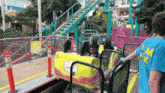 a man wearing a blue shirt that says em on it is standing next to a roller coaster