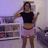 a woman in a black crop top and pink shorts stands in front of a toy shelf