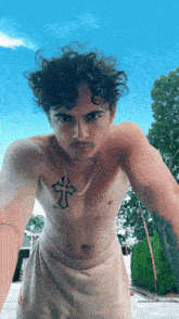 a shirtless man with a cross tattoo on his chest looks at the camera