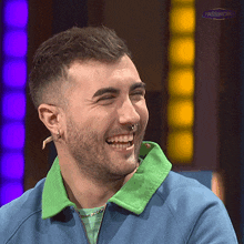 a man with a beard and nose ring is laughing and wearing a blue jacket