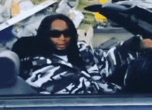 a man wearing sunglasses is sitting in a car with his hood up .