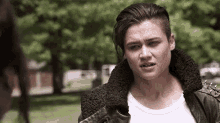 a woman with a shaved head and a leather jacket is standing in a park talking to another woman .