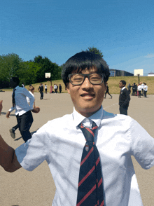 a boy wearing glasses and a striped tie stands in a playground