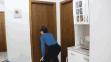 a woman in a blue shirt and black pants stands in a kitchen