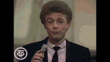 a man in a suit and tie is holding a glass of wine and making a funny face .