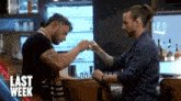 two men are sitting at a bar holding hands and toasting .