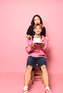 a man sitting on a stool holding a cake and a woman behind him