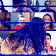 a woman with blue hair is in a wrestling ring with a crowd watching