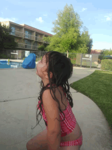 a little girl in a red and white striped bathing suit is standing in front of a pool