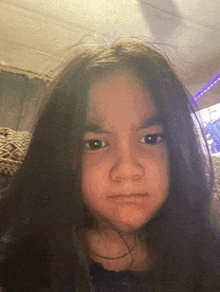 a young girl with long hair is making a funny face while sitting on a couch .