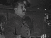 a man with a mustache is standing in front of a microphone in a black and white photo with russian writing on the bottom right