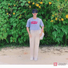 a person wearing a blue levi 's shirt standing in front of a bush