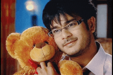 a man wearing glasses holds a teddy bear with a red bow