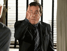 a man in a suit and tie holds his hand to his forehead