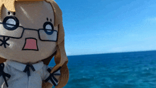 a stuffed doll with glasses and a star in her mouth is standing in front of the ocean