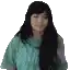 a woman with long black hair is wearing a green shirt and looking at the camera .
