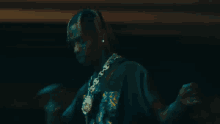 a man is singing into a microphone in a dark room while wearing a necklace .
