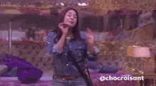 a woman in a denim jacket is dancing in a room with purple blankets .