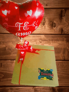 a heart shaped balloon that says te amo is sitting on top of a gift box