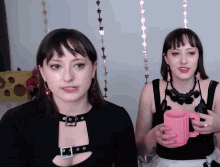 two women are standing next to each other and one of them is holding a pink mug
