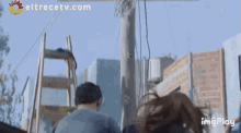 a man and a woman are walking down a street with eltrecetv.com written in the corner