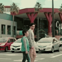 a man and a boy are walking across a street in front of cars .