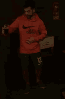 a man wearing an orange nike hoodie and green shorts is holding a drink