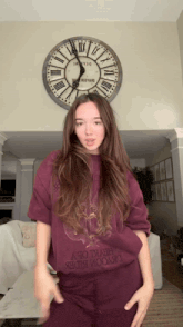 a woman in a purple shirt stands in front of a clock that says " buzzard " on it