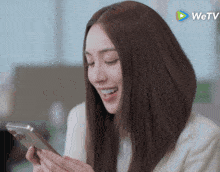 a woman is smiling while looking at her phone with a wetv logo in the corner