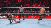 two men are wrestling in a wrestling ring with a referee and a crowd watching .