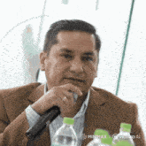 a man in a suit holds a microphone in front of bottles of water