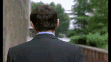 a man in a suit and blue shirt is walking across a bridge .