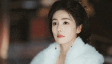 a woman wearing a white fur coat and earrings is looking at the camera .