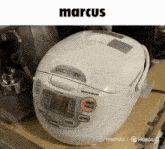 a white rice cooker sits on a wooden shelf under a sign that says marcus