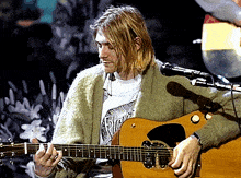 a man playing a guitar with a shirt that says ' nirvana ' on it