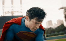 a man in a superman costume with a red cape is standing on a baseball field .