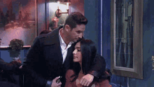 a man is hugging a woman in a room with a picture on the wall behind them