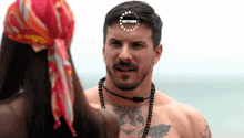 a man with a tattoo on his chest looks at a woman with a red head scarf