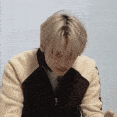 a young man with blonde hair is wearing a black and white sweater and looking down .
