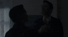 a man in a suit and tie holds another man 's neck in a dark room
