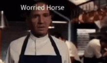 a man wearing an apron is standing in a kitchen with the words worried horse written on the screen .