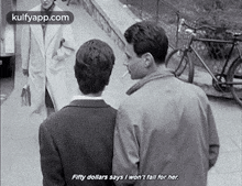 a couple of men standing next to each other on a sidewalk . one of the men is smoking a cigarette .