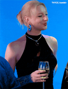 a woman in a black dress is holding a glass of wine and smiling