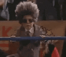 a young boy in a wig and sunglasses is standing in a boxing ring .