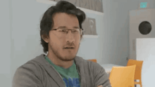 a man with glasses and a beard is sitting at a table with his arms crossed and looking at the camera .