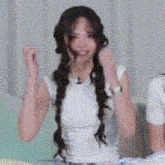 a woman with long braids is wearing a white shirt and sitting on a bed .