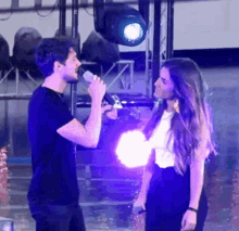 a man singing into a microphone while a woman looks on