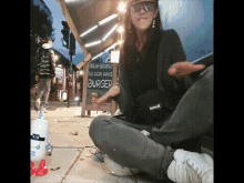 a woman sits on the sidewalk in front of a sign for english breakfast egg bacon sausage burger