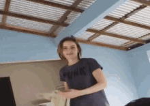 a woman in a pink shirt is standing in a room with a blue wall and a wooden ceiling .