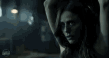a woman is standing in a dark room with her arms behind her head .